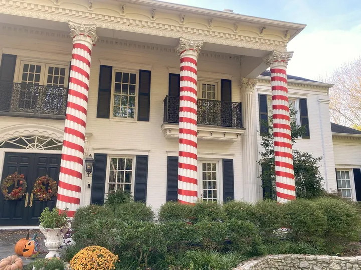 A large white-columned North Texas property with each column wrapped in red and white candy-cane lighting