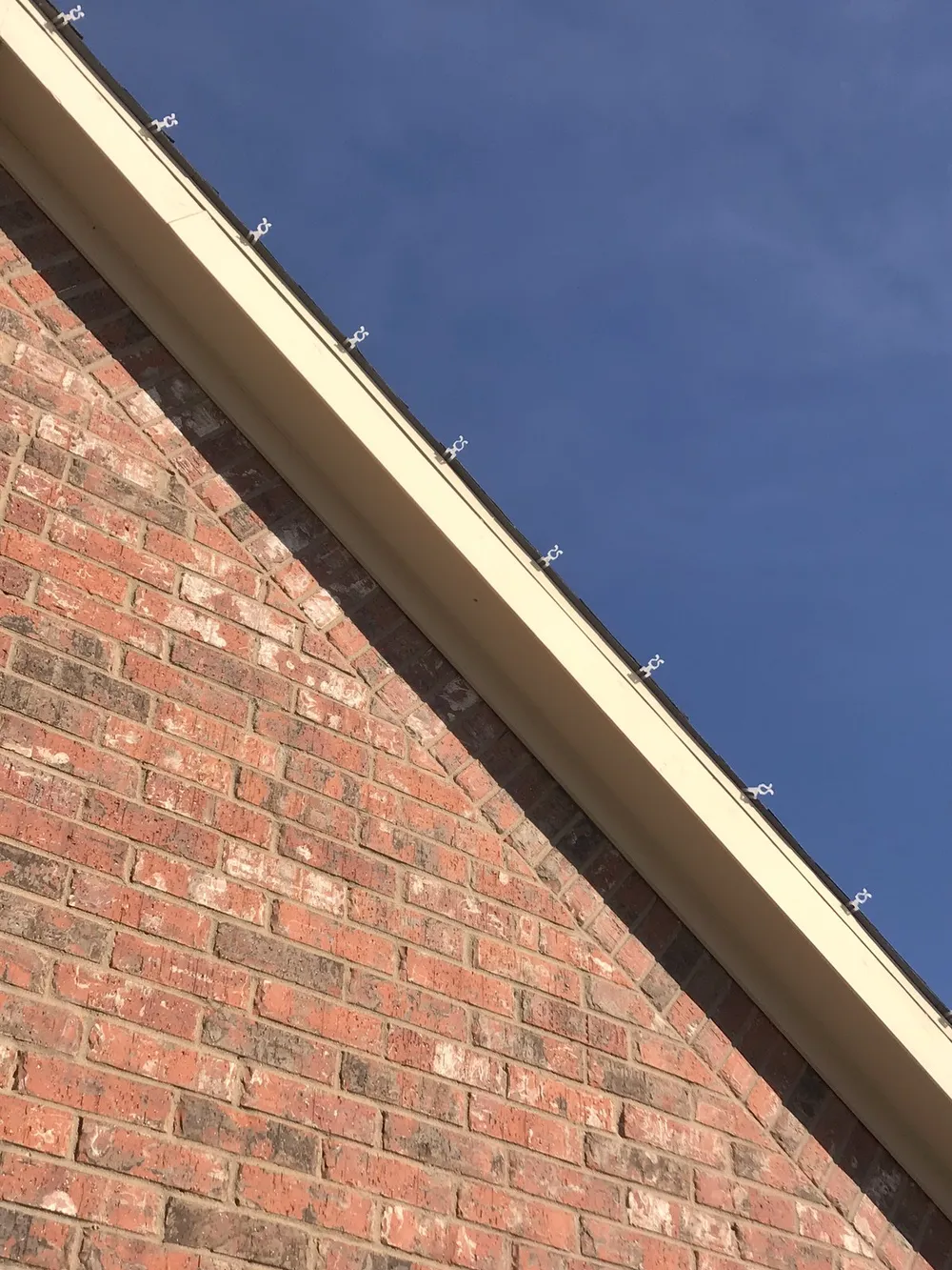 A close-up of Christmas light clips seated along the roofline of a North Texas brick home