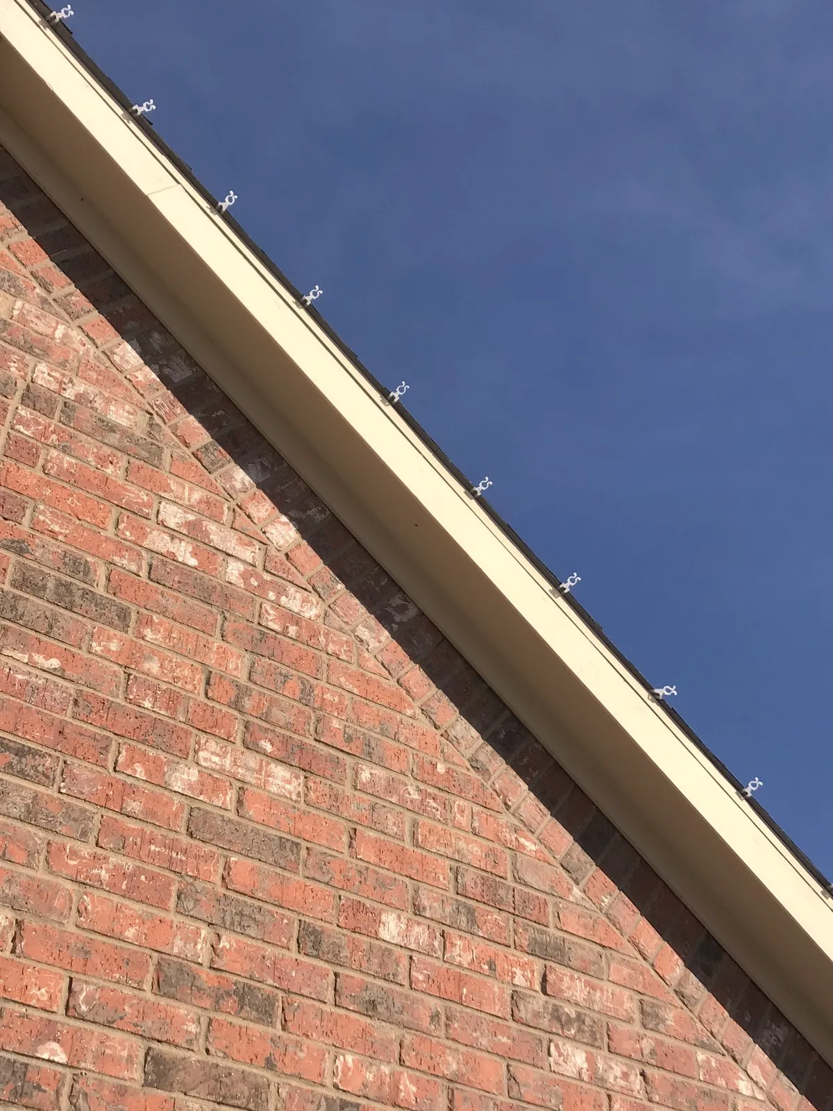 A close-up of Christmas light clips seated correctly along a brick roofline