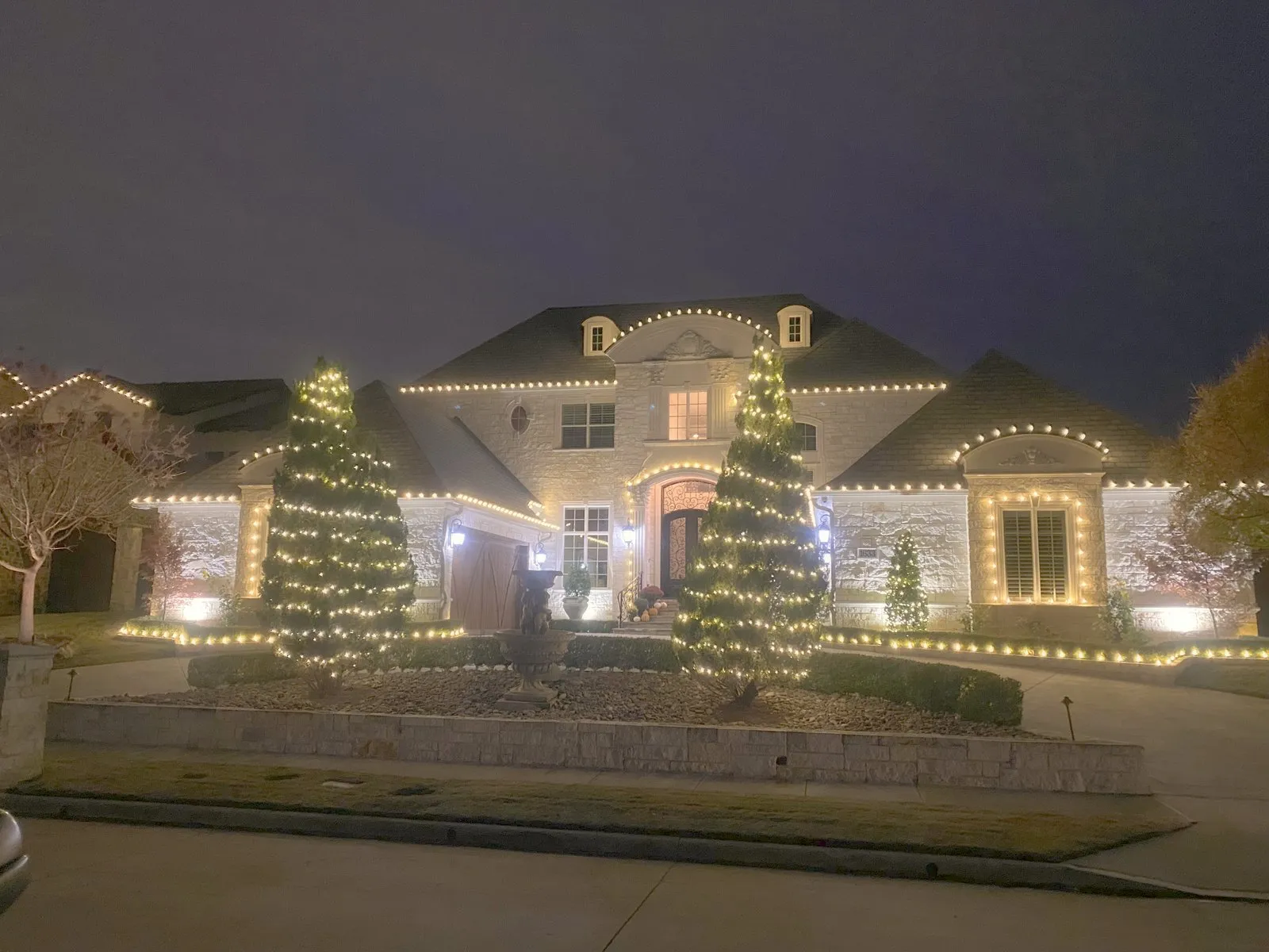 A North Texas estate lit in warm white with wrapped trees along the driveway