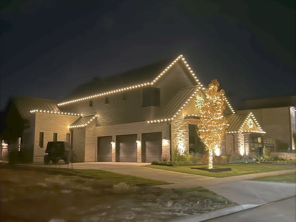 A two-storey North Texas home lit at dusk with wrapped trees