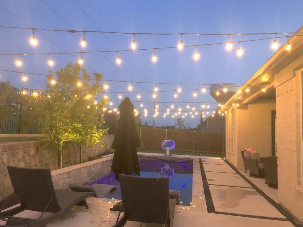 Bistro string lights over a patio and pool at dusk before an event